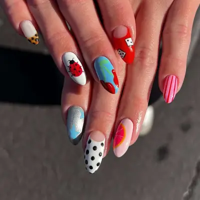 Hands with creatively designed manicured nails featuring a mix of patterns and themes, such as dots, fruit, and gradients