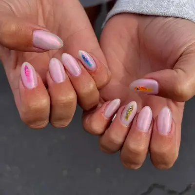 Hands with manicured nails showing small colored fish nail art on a neutral background