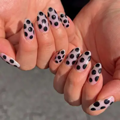 Close-up of hands with sheer nails featuring black polka dot design