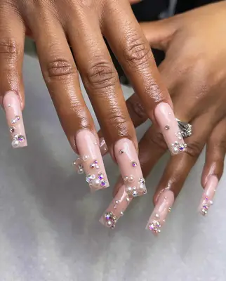 Long square nails with pink nude polish embellished with rhinestones and pearls