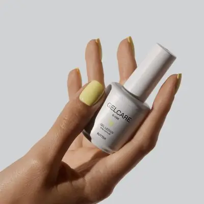 A hand holding a bottle of Gelcare nail polish with yellow-painted nails