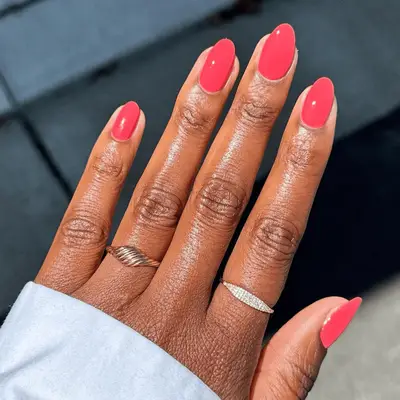 A hand holding a bottle of pink nail polish with neatly manicured nails