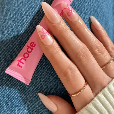 Long almond shaped nails with sheer glittery polish and pink bows on light skin tone