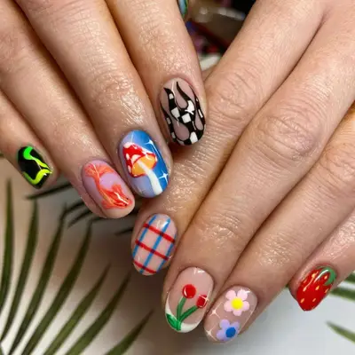 Nails with different designs on each finger. From left to right: black and neon design, Koi fish, magic mushroom, fire in black and white tiles, red and blue plaid, cherries on a French base, flowers with sparkles, and a strawberry.