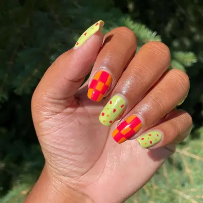 Red and orange checker nails alternated with a yellow-green base with red and orange dots.