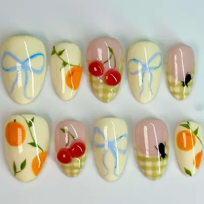 Press-on nails with bows, oranges, green plaid French tips with 3D cherries, and green plaid French tips with ants.