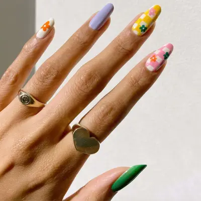 White nail with orange flower, purple nail, yellow and white tiled nail with flower decals, pink and white tiled nails with flower decals, and green nail.