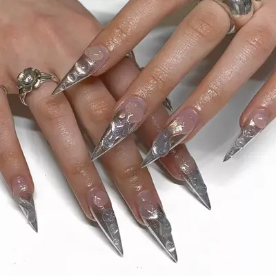 Close up of long stiletto shaped nails with silver sparkles and 3D dew drop nail art.