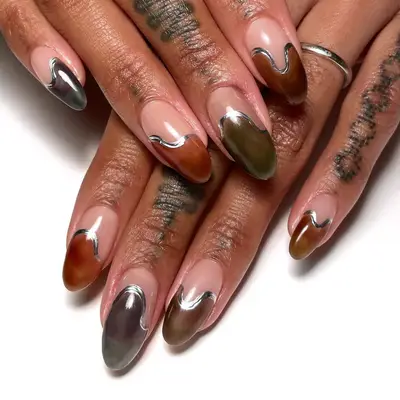 A close up of oval nails with earth tone French tips outlined with silver polish.