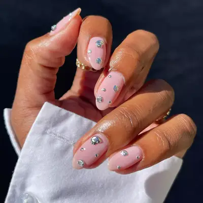 A close up of nude nails with silver 3D seashell gems.