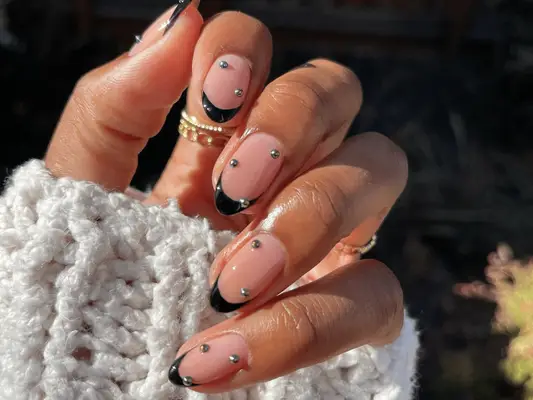 A clear nail polish manicure with black French tips and silver ball stud embellishments