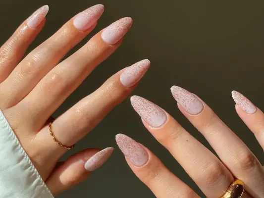 Two hands with a pale pink manicure that features glitter ombré