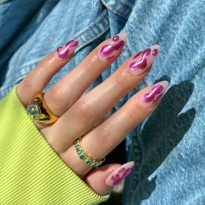 Open hand wearing gold rings and green sweater with bright pink chrome nails