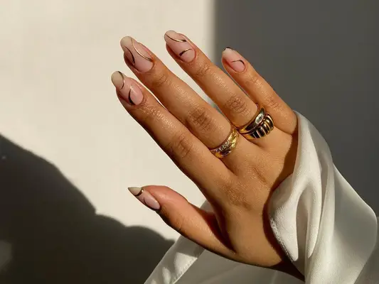 Manicure with neutral base and gold curve designs