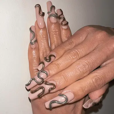 Nude, long square nails with gold and silver 3D squiggles.