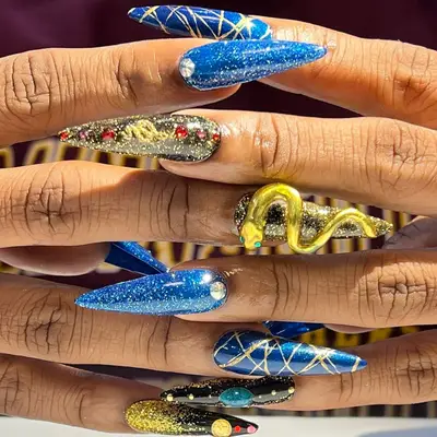 Glittery, intricate mismatched nails with gems, swirls, and a 3D snake in shades of blue, gold and black.