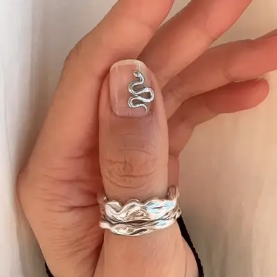 A nude thumb manicure with a 3D silver snake.