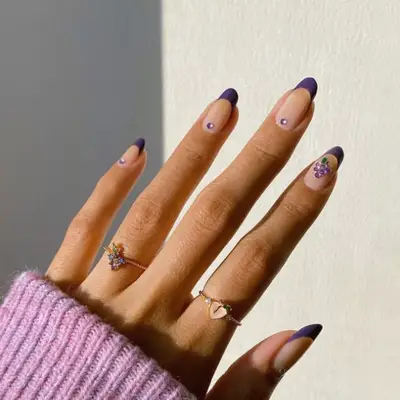 Purple French manicure with purple gem and a bunch of grapes made out of purple gems.