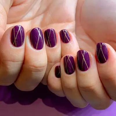 Dark purple nails with thin gold geometric lines.