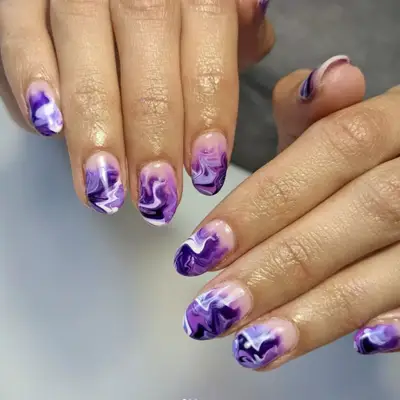 Shades of purple and white in water color swirls on a manicure.