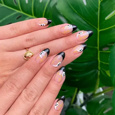Almond shaped nails with black French tips, orange plaid, and ghost nail art.
