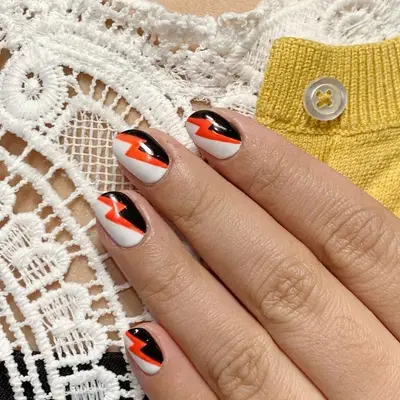 White, black, and orange lightning bolt nail design