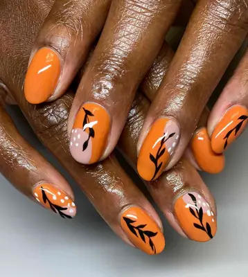 Short round nails with wavy orange nail polish and black floral, white dot nail art.