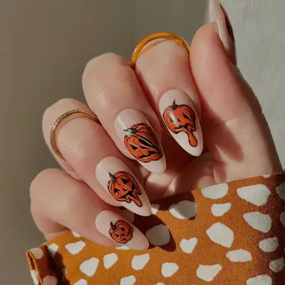 Close up of milky white nails with melted carved pumpkin motifs.