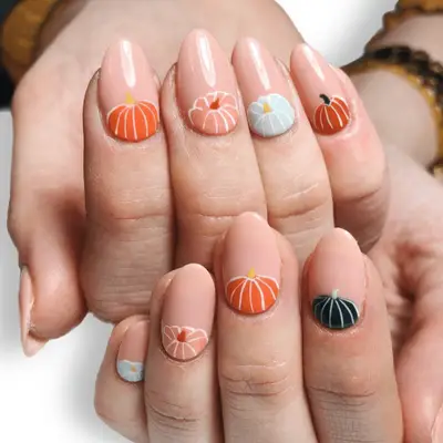 Close up of nude-pink nails with pastel pink, blue and orange pumpkins at the cuticle.