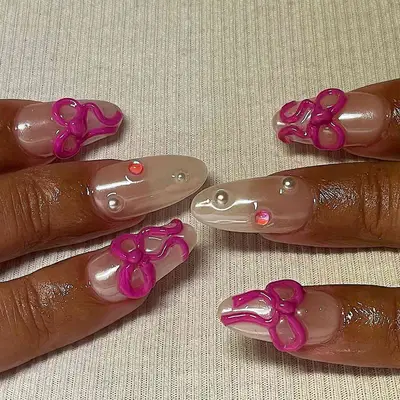 Shiny chrome nails with hot pink bows and multicolored gems