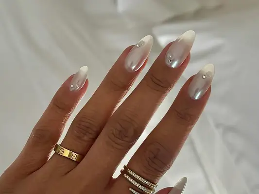 A white chrome manicure with pearl and rhinestone accents