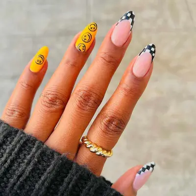 A manicure with checkerboard French tips and yellow accent nails with Blink-182 smiley faces