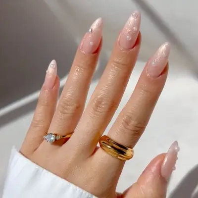 Hand with pearl-dotted nails featuring a golden ring and a diamond ring