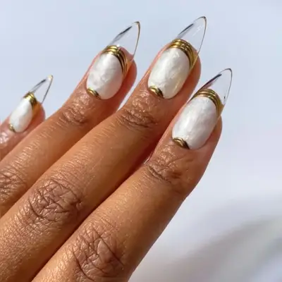 A hand with long fingernails featuring a Cult Gaia-inspired pearl design and gold accents