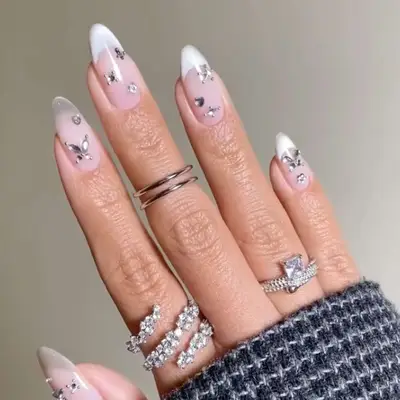 Hand showcasing a decorated French manicure with gemstones and multiple rings