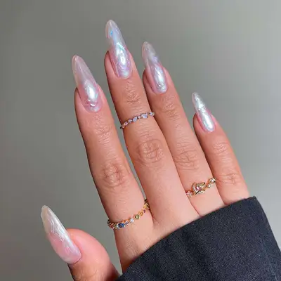 Close-up of a hand with long nails featuring a textured mother-of-pearl design, adorned with multiple delicate rings