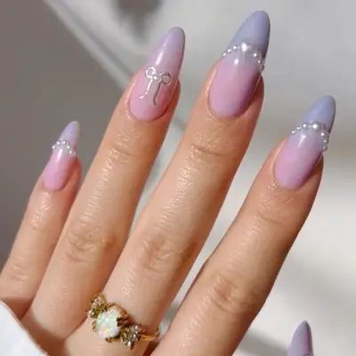 Hand with pastel gradient nails, pearl accents, and a bow-like ornament