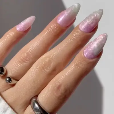 A hand with long, glossy nails and soft gradient design, wearing minimalist rings