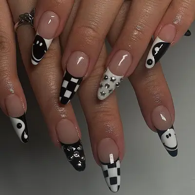 Black and white nails with yin and yang, checkered print, smiley face, and studded gem French tips