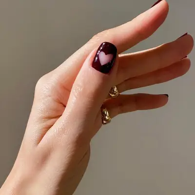 Close-up of manicure with dark burgundy polish and negative space heart nail design