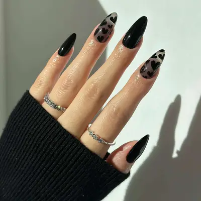 Manicure with alternating solid black nails and sheer smoky nails with black hearts