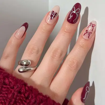 Close-up of manicure with burgundy and silver bows, French tips, hearts, and 