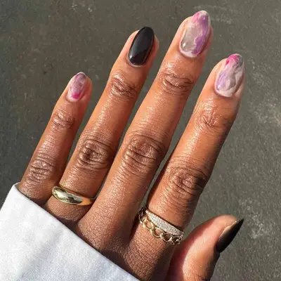 Manicure with two black nails and three smoky pink, purple, and gray marble nails