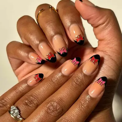 Close-up of manicure with neutral base, black French tips, and red and pink bow designs