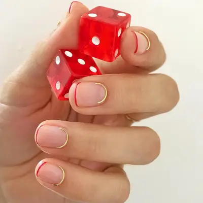 Manicure with minimal red French tips and crescent-shaped gold wire at base