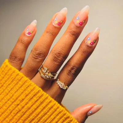 Glossy neutral translucent manicure with multicolored flower designs at cuticle