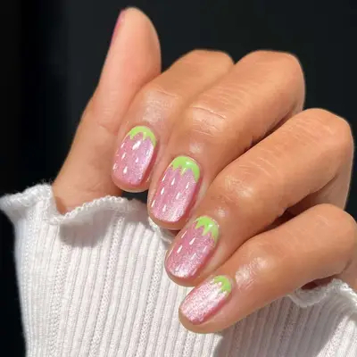 Hand with strawberry-themed nail art design, green tips resembling leaves