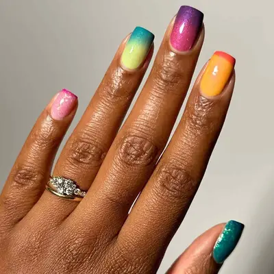 A hand with multicolored gradient nail polish and a ring with a decorative stone
