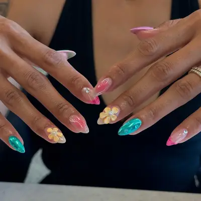 Person displaying a manicure with elaborate design including floral patterns on their nails, wearing rings on fingers