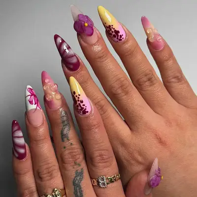 Hand with decorated nails featuring various artistic floral and color patterns
